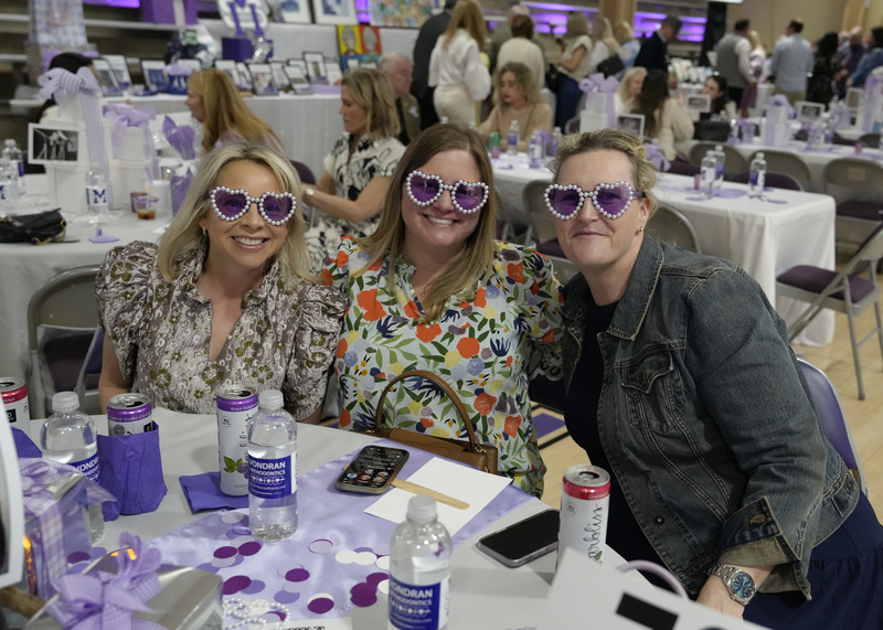three event guests seated at table with purple heart-shaped sunglasses on