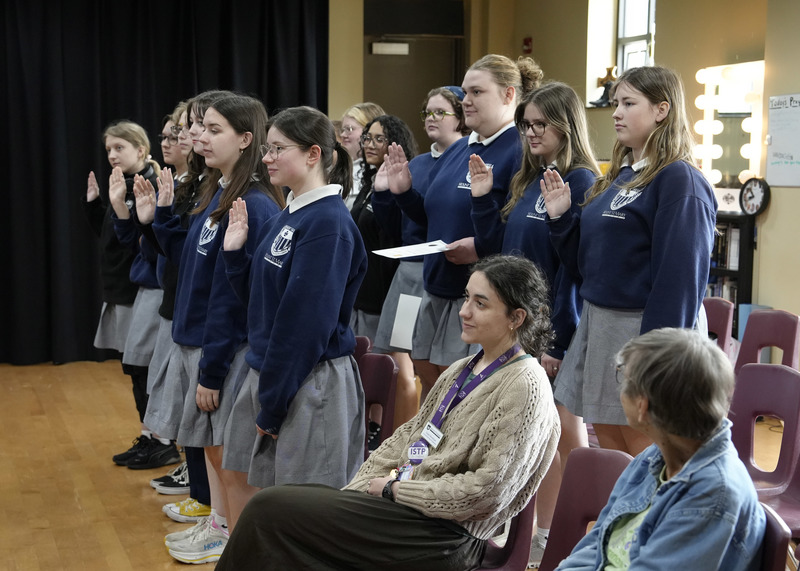 group of students standing up with hands raised while reciting a pledge