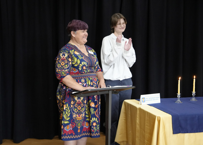 adult and student standing at podium smiling and clapping