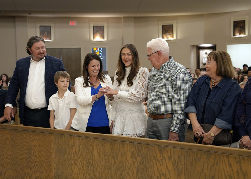 family members presenting student with senior ring during Mass inside a church