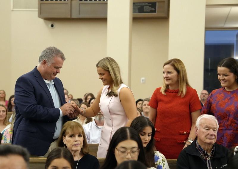 family members presenting student with senior ring during Mass inside a church