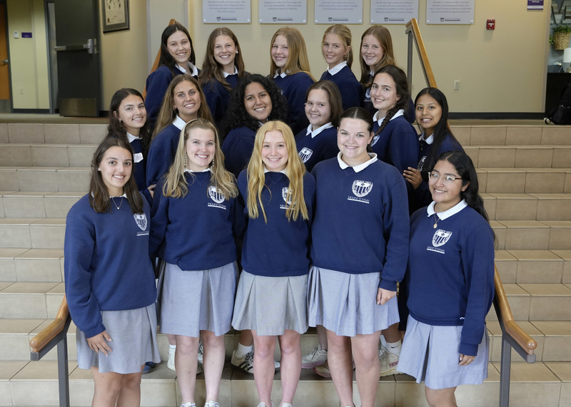large group of female students in school uniform standing on steps in school foyer