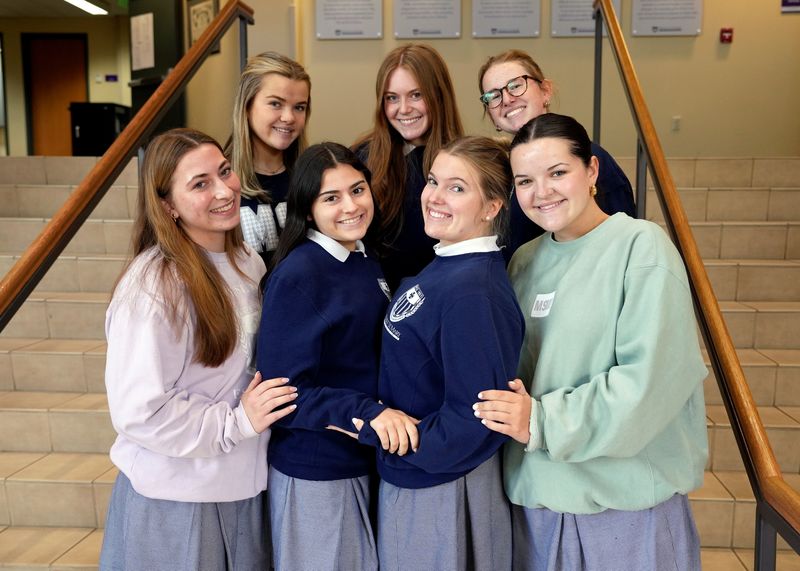 seven female students standing on the steps in the school's foyer smiling at the camera