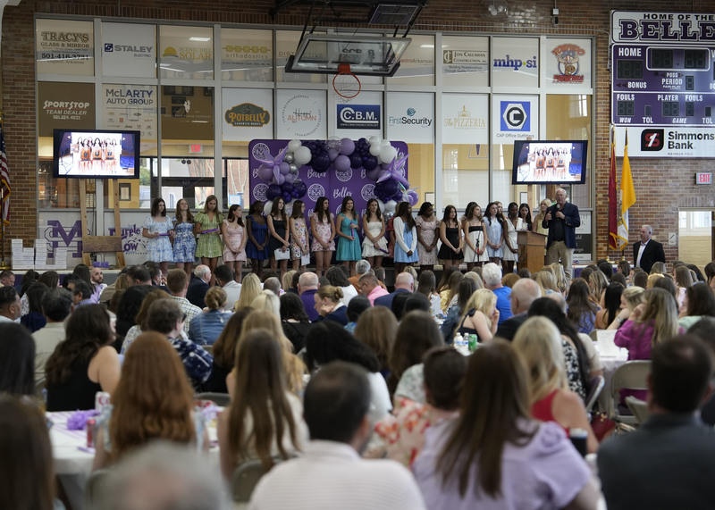 group of female students standing on stage while receiving recognition from speaker at podium