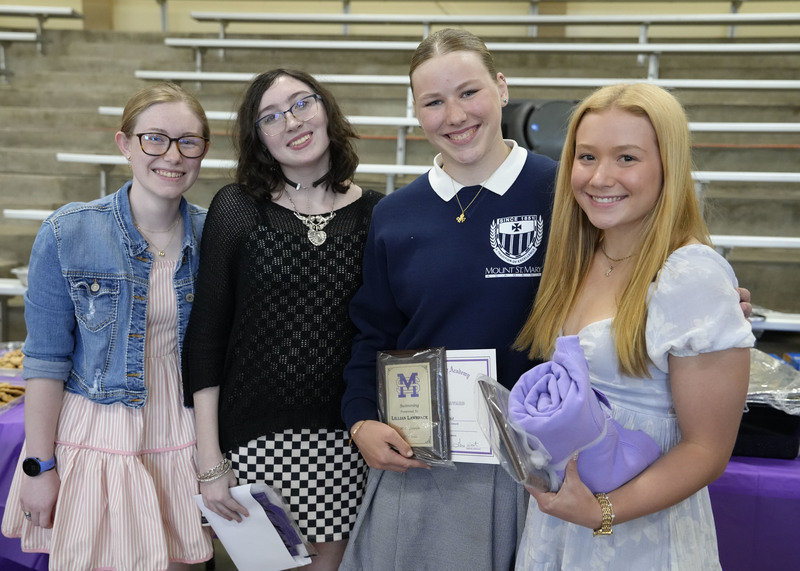 four students holding awards and smiling at the camera