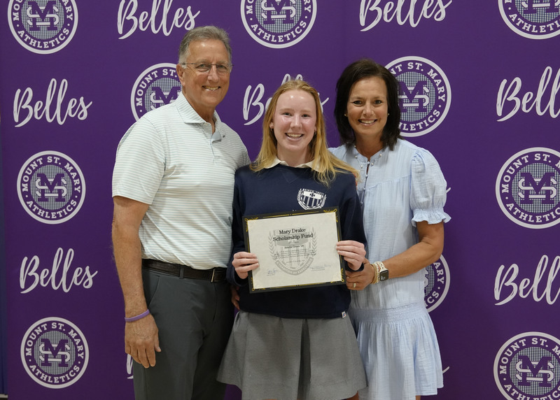 a student and two adults standing in front of a purple backdrop, holding an award certificate, and smiling at the camera