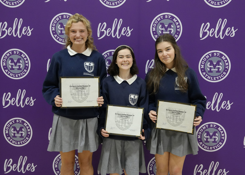 three students standing in front of a purple backdrop, holding award certificates, and smiling at the camera