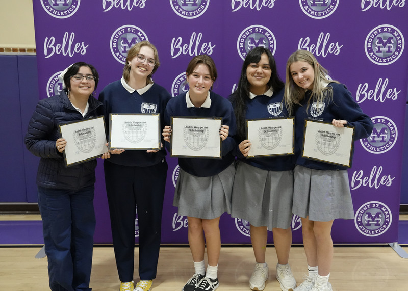 five students standing in front of a purple backdrop, holding award certificates, and smiling at the camera