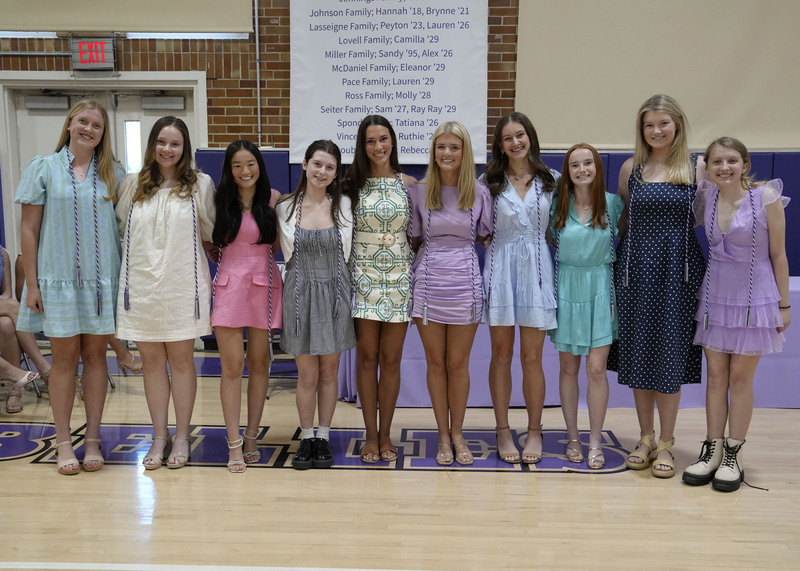 ten students with purple and white graduation cords smiling at the camera