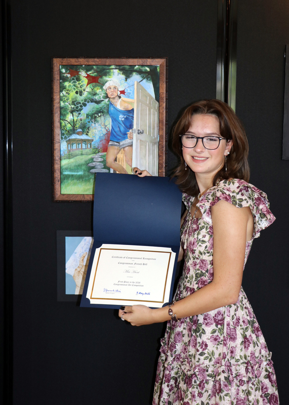 student holding award certificate in front of winning artwork