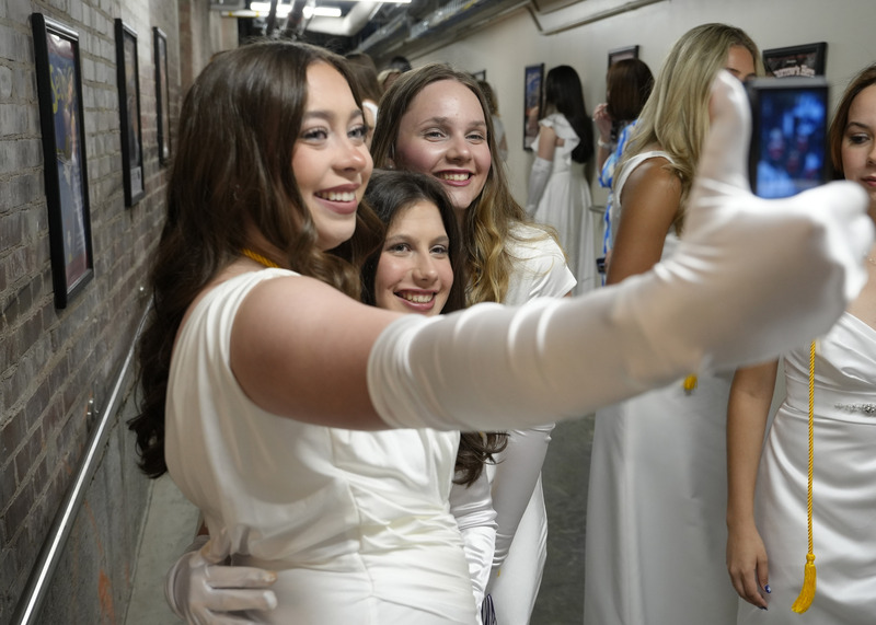 three young women in long white gowns and white gloves taking a selfie