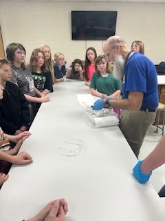 middle school kids watching a bearded teacher dissect a frog
