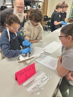 middle school kids in goggles and gloves dissecting a frog a male teacher watches