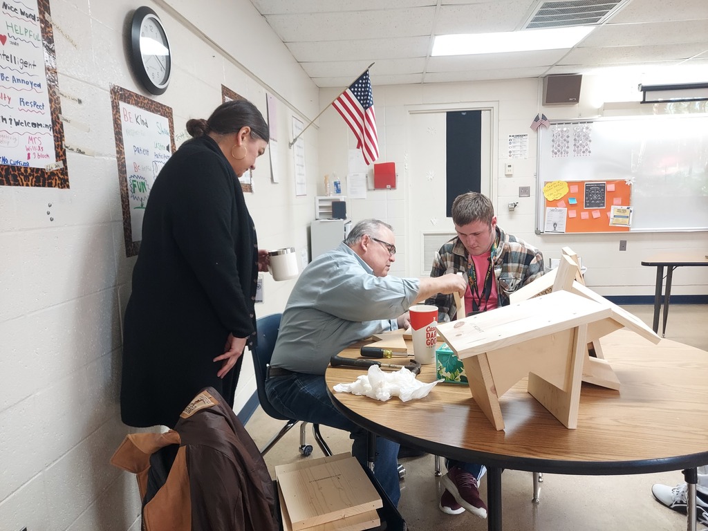 high school boy building birdhouse with the help of two adult volunteers