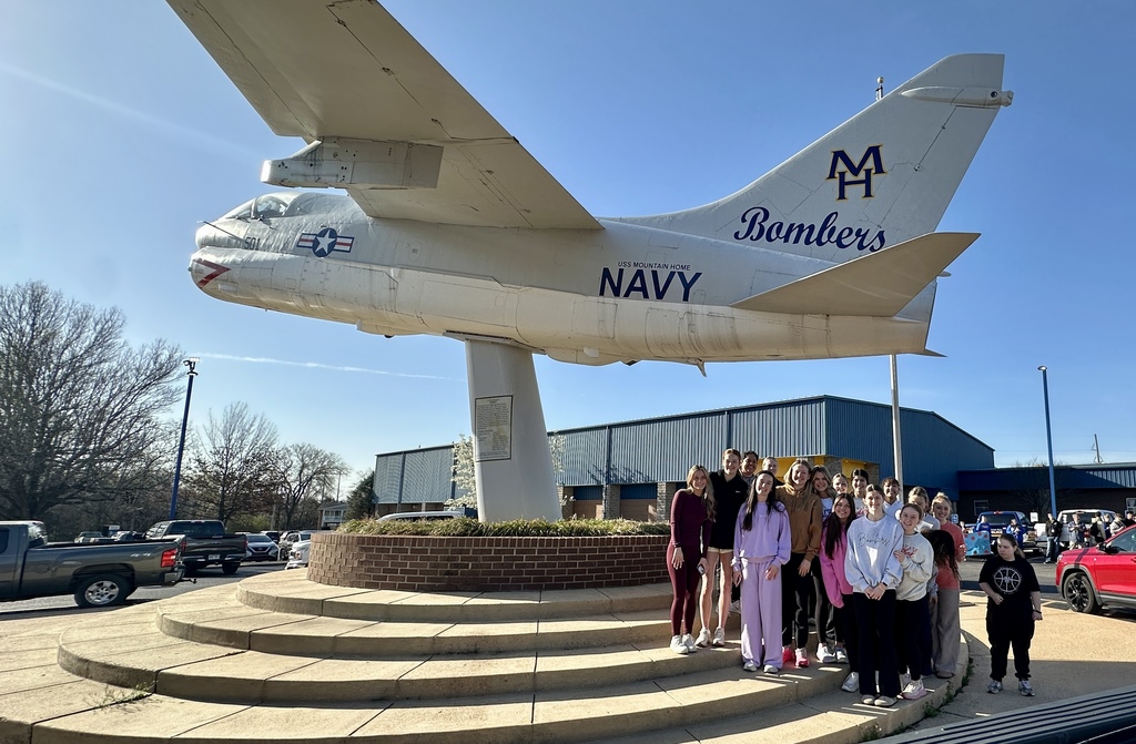 Girls basketball team standing in front of the Bomber Plane on campus