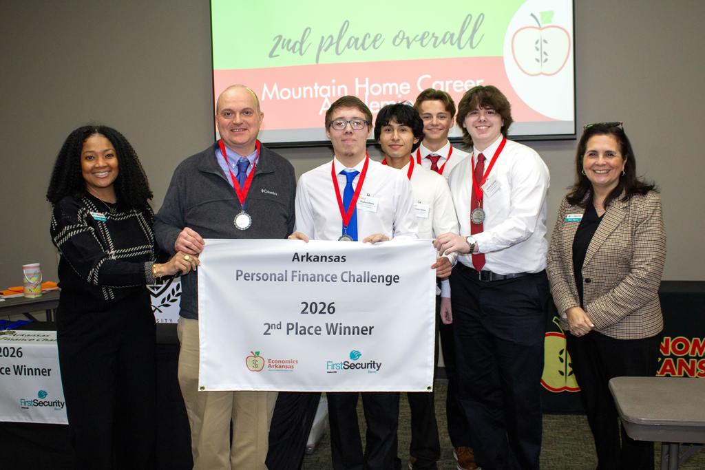 students with teacher and banner as well as two female representatives from Economics Arkansas