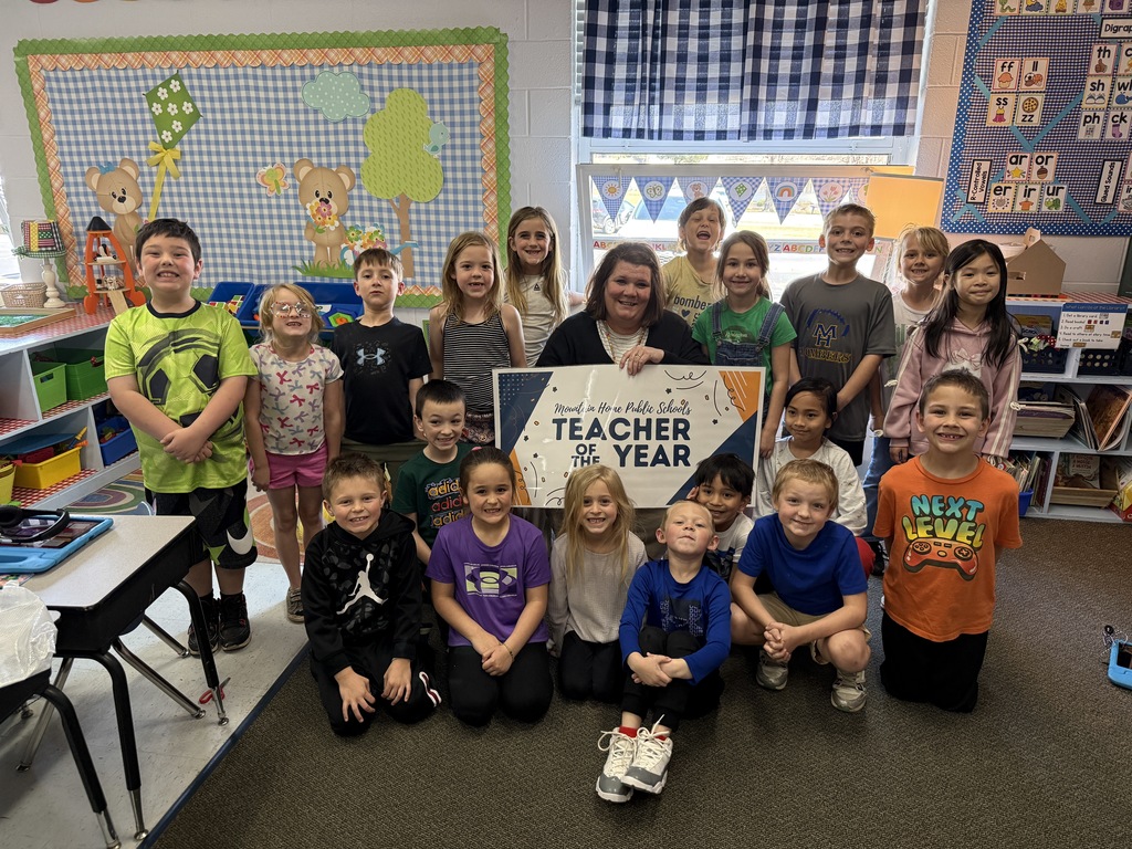 MRs. Seawright holding a teacher of the year sign with her first grade class surrounding her