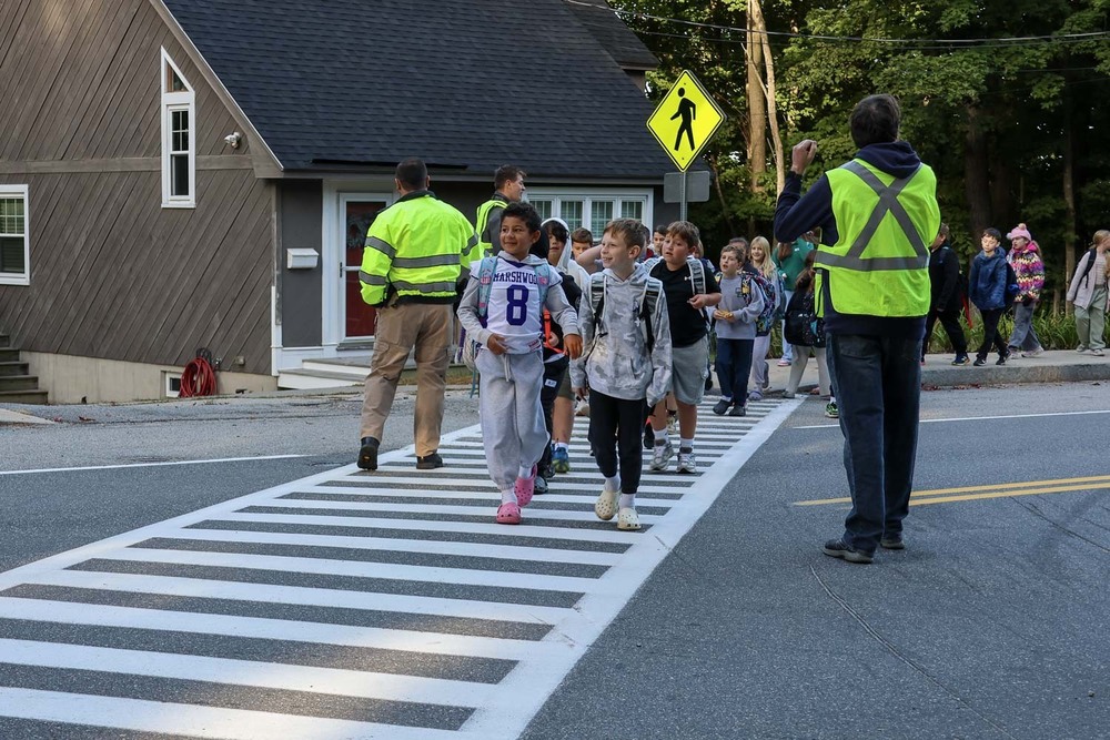 Students from the Jerry Burnell Great Works school cross the road with the help of their teachers during Walk to School Day .