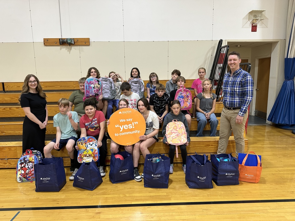 A group of students sitting with two adults who have donated bags of school supplies to their school.