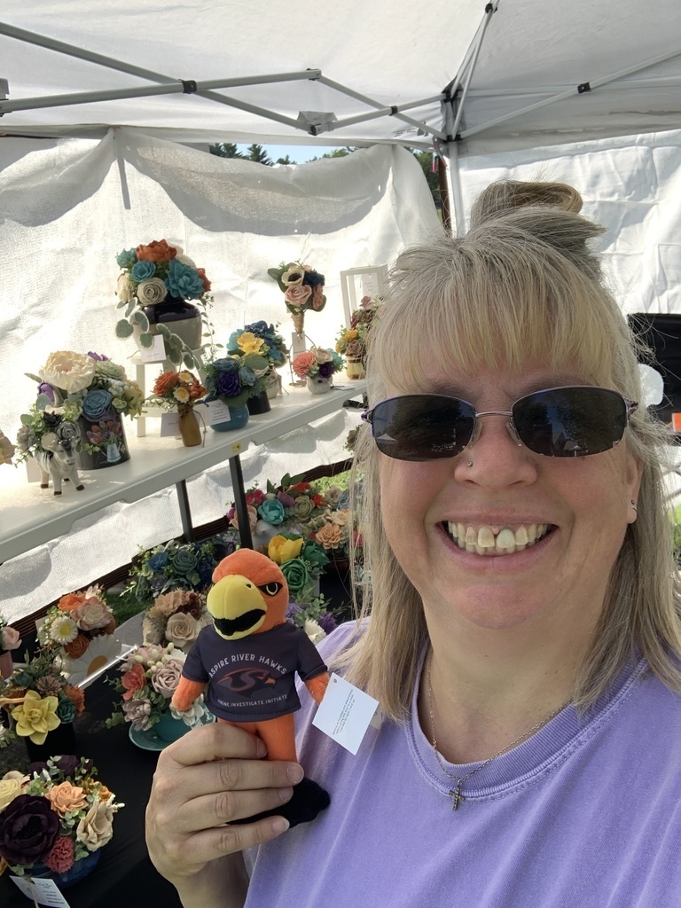 Teachers outside with River Hawk plushie in front of flowers