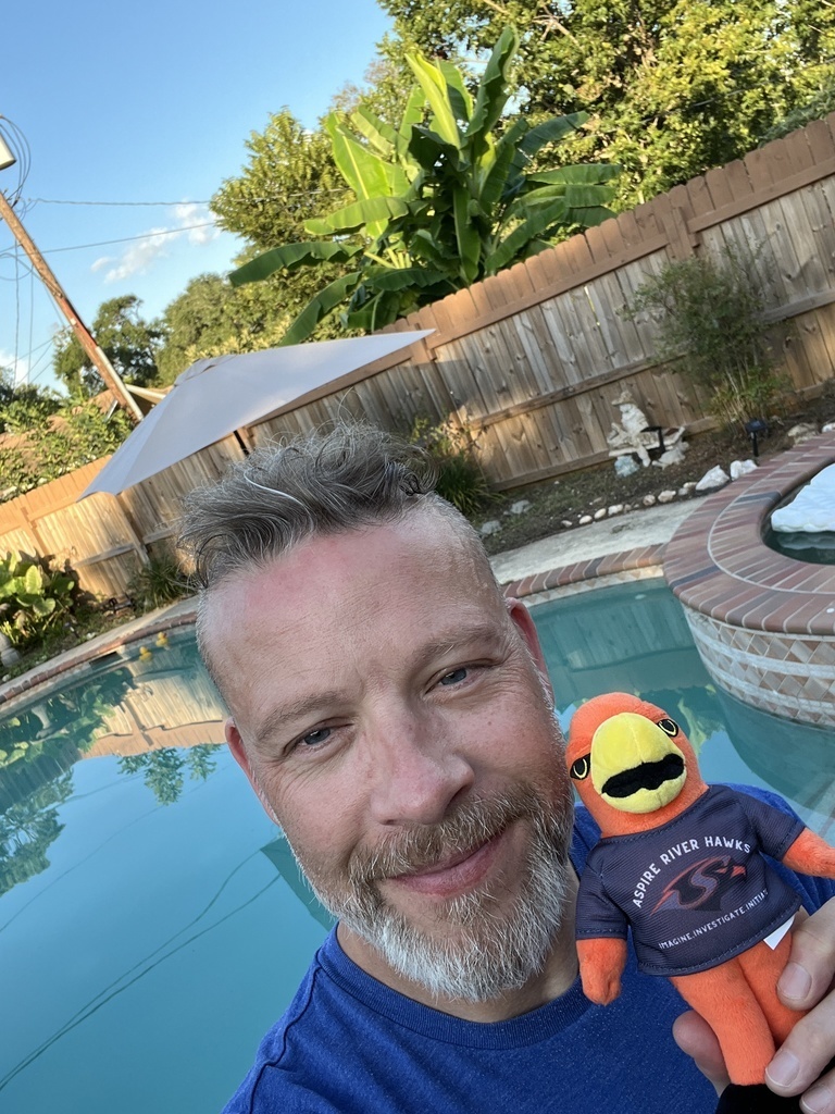 Teacher outside with River Hawk plushie in front of pool