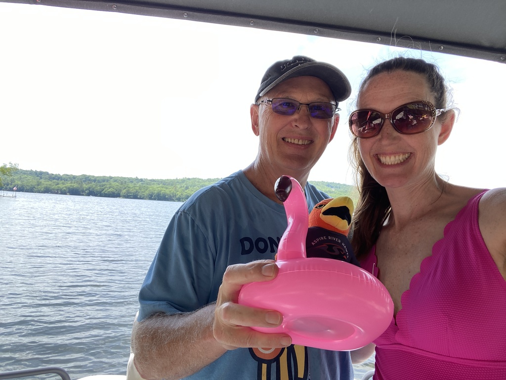 Teachers outside with River Hawk plushie and mini flamingo in front of lake