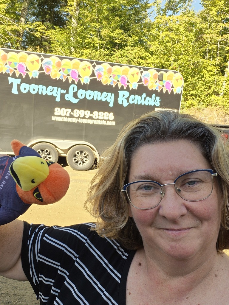 Teacher outside with River Hawk plushie in front of Tooney Looney Rentals truck