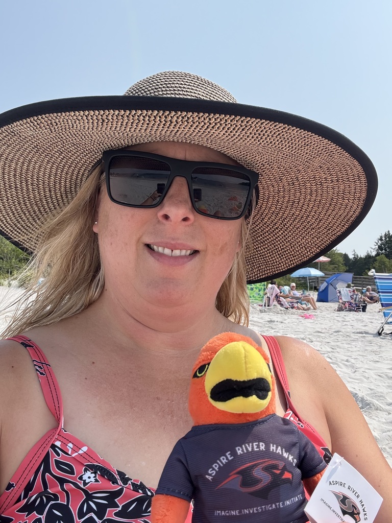 Teacher outside with River Hawk plushie at beach