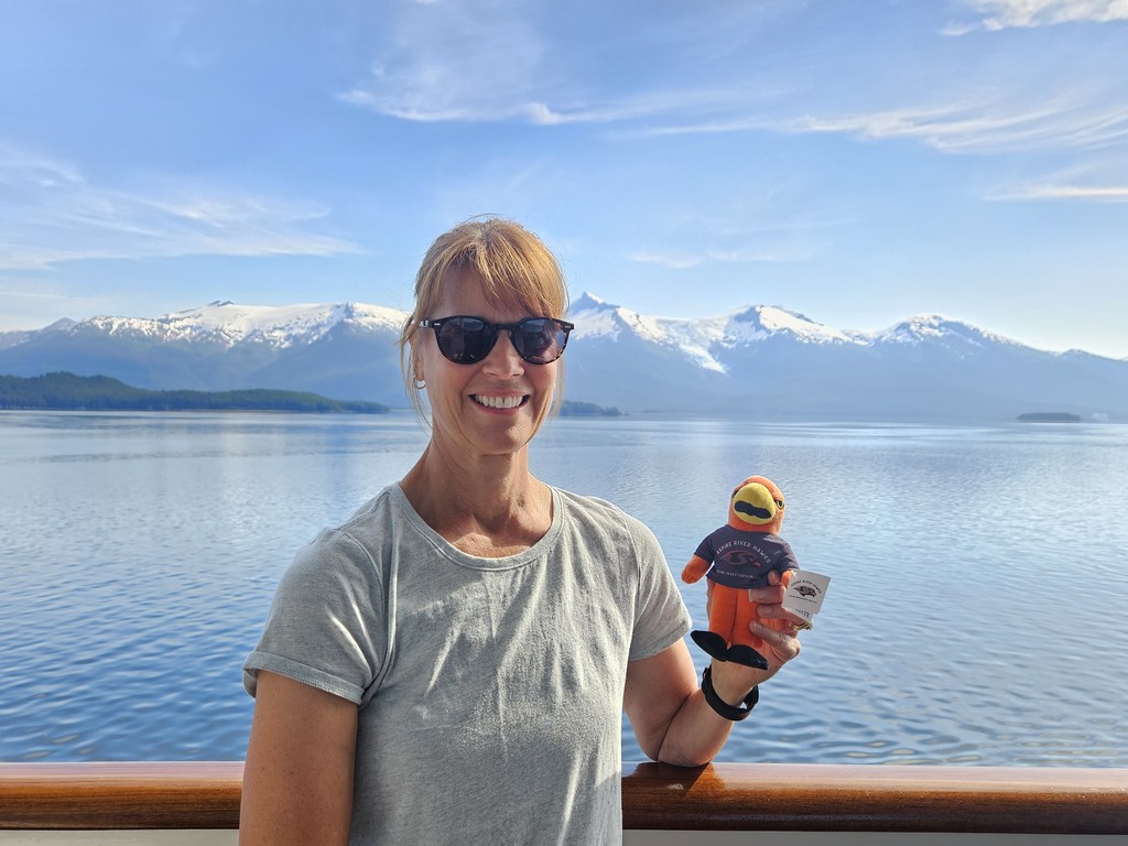 Teacher outside with River Hawk plushie in front water and mountains