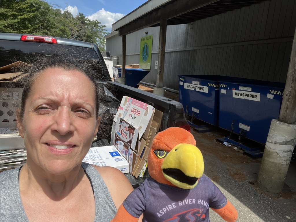 Teacher outside with River Hawk plushie in front of recycling center