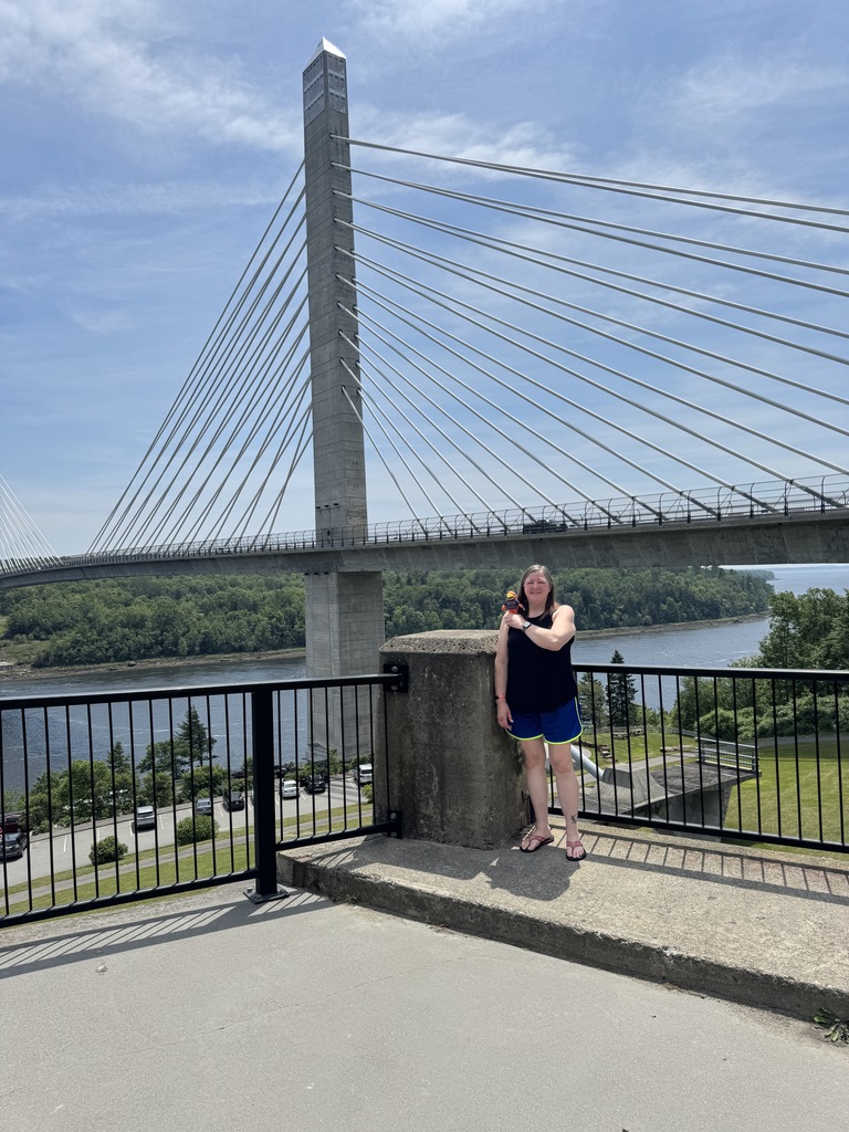 teacher with river hawk plushie in front of bridge