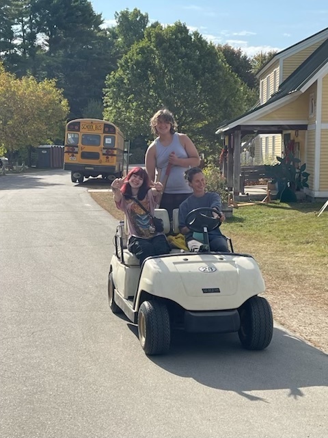 Three students outside riding on a golf cart