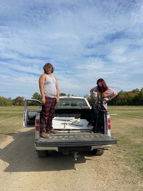 Two students outside standing on the back tailgate of a white pickup truck