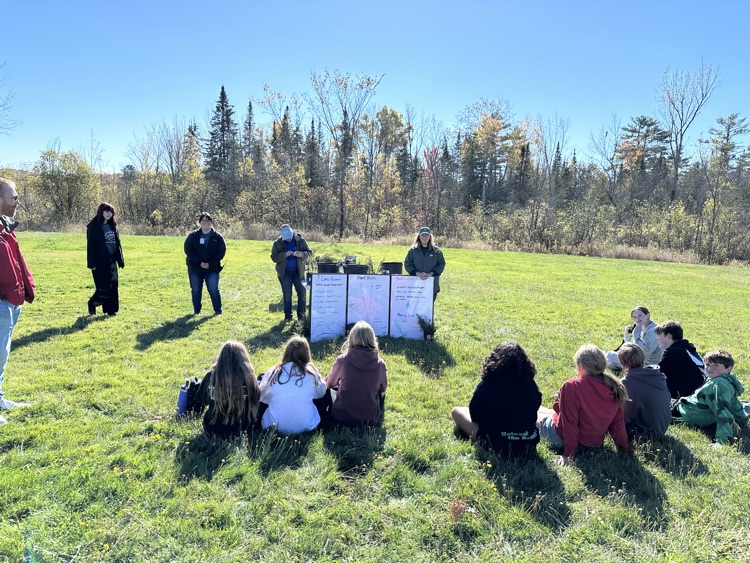 students sitting on the ground outside viewing a presentation about erosion