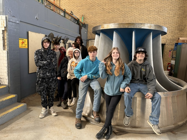 students posing on a large hydroelectric turbine