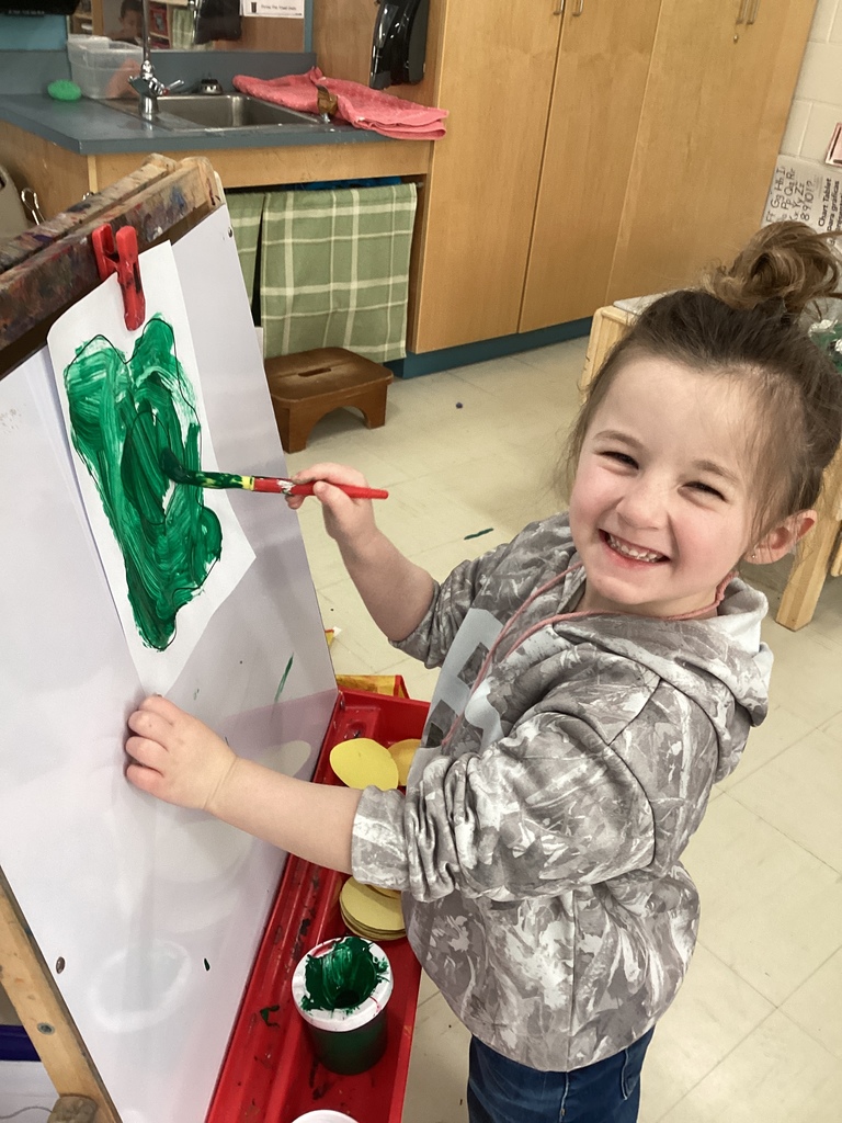 A girl painting a green spot on an easel. 
