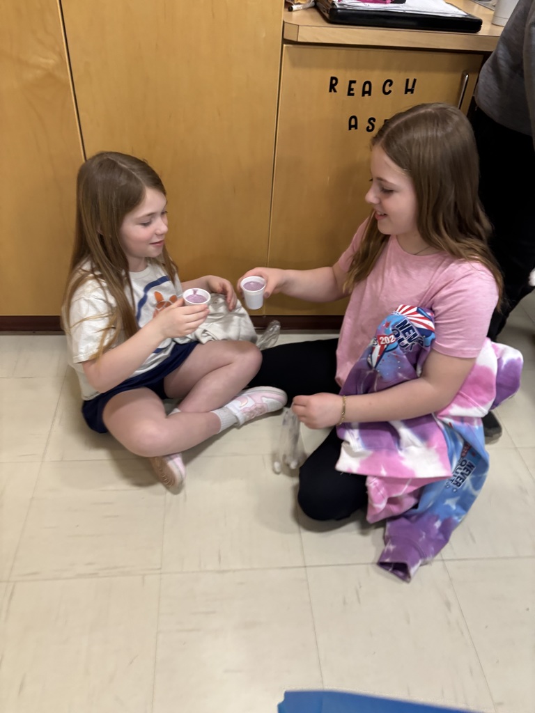 Two girls drink from white plastic cups.