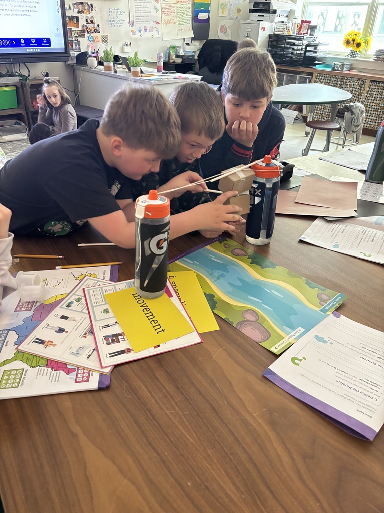 Three young boys gather around a project on a table. 