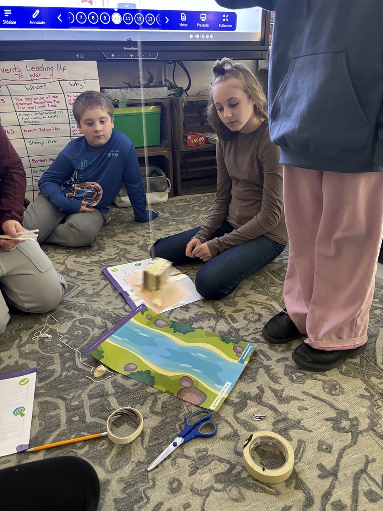 Students work on the rug with materials. 