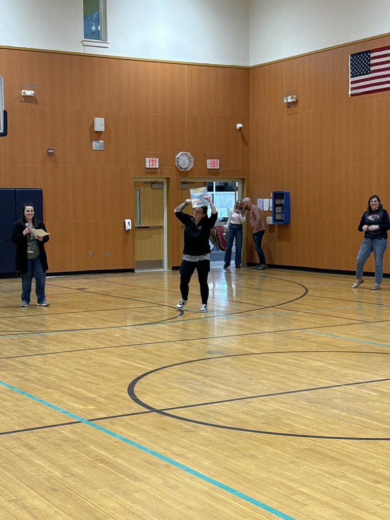 Teacher holds up a book in a gym.