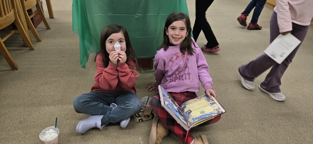 Two girls sitting on floor with book and sticker.