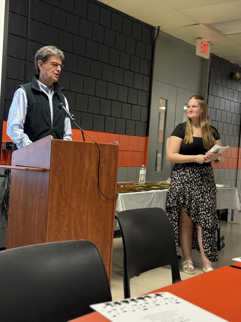 speaker at podium in cafeteria, high school student holding certificates and looking at speaker