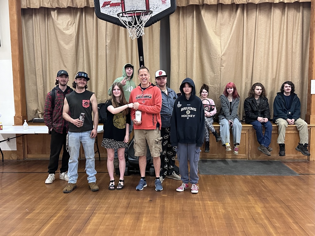 Teacher holding cup posing with students under basketball net in school gym