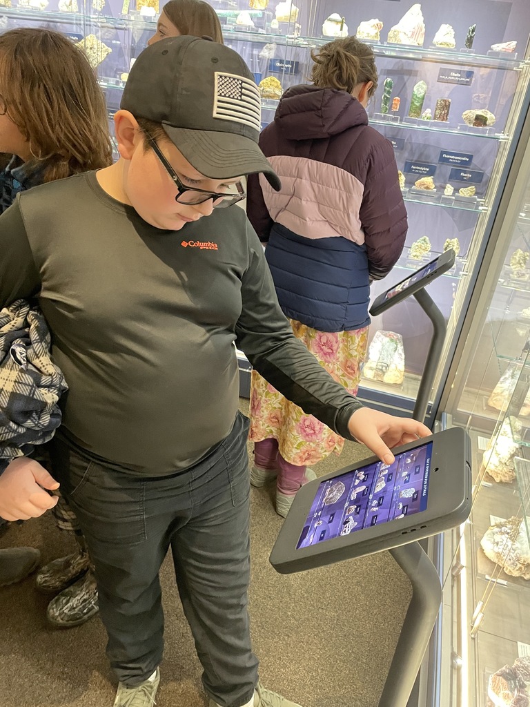 student interacting with tablet screen in front of display cases of minerals and gems in museum setting