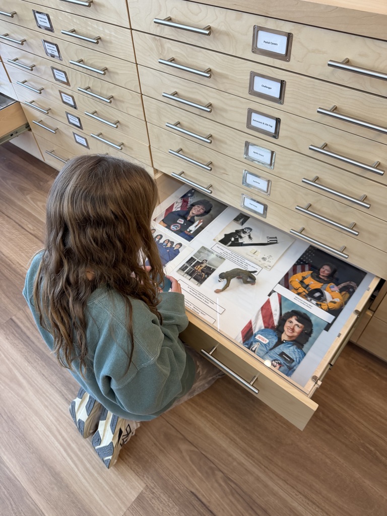 middle school student with long hair looking at pictures of female scientists in a drawer in filing cabinet