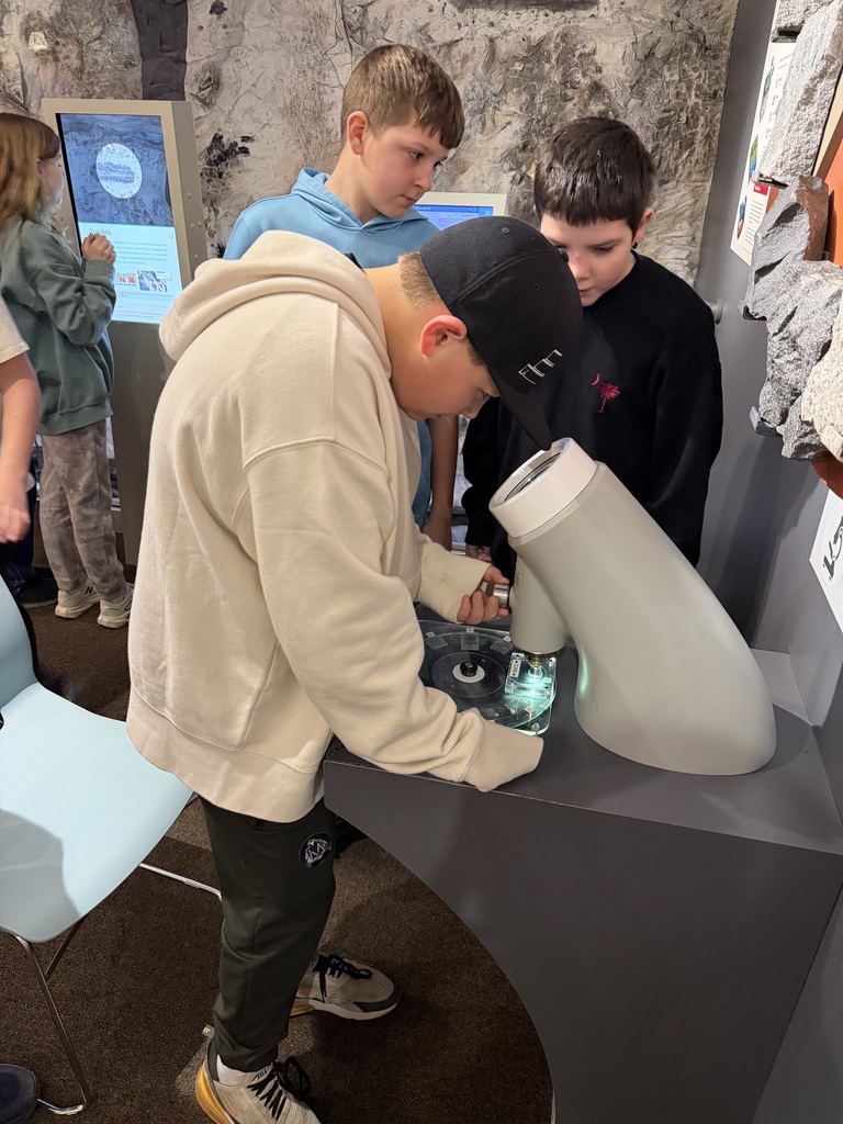 student interacting viewing minerals and gems under microscope in museum setting, more students looking on in the background
