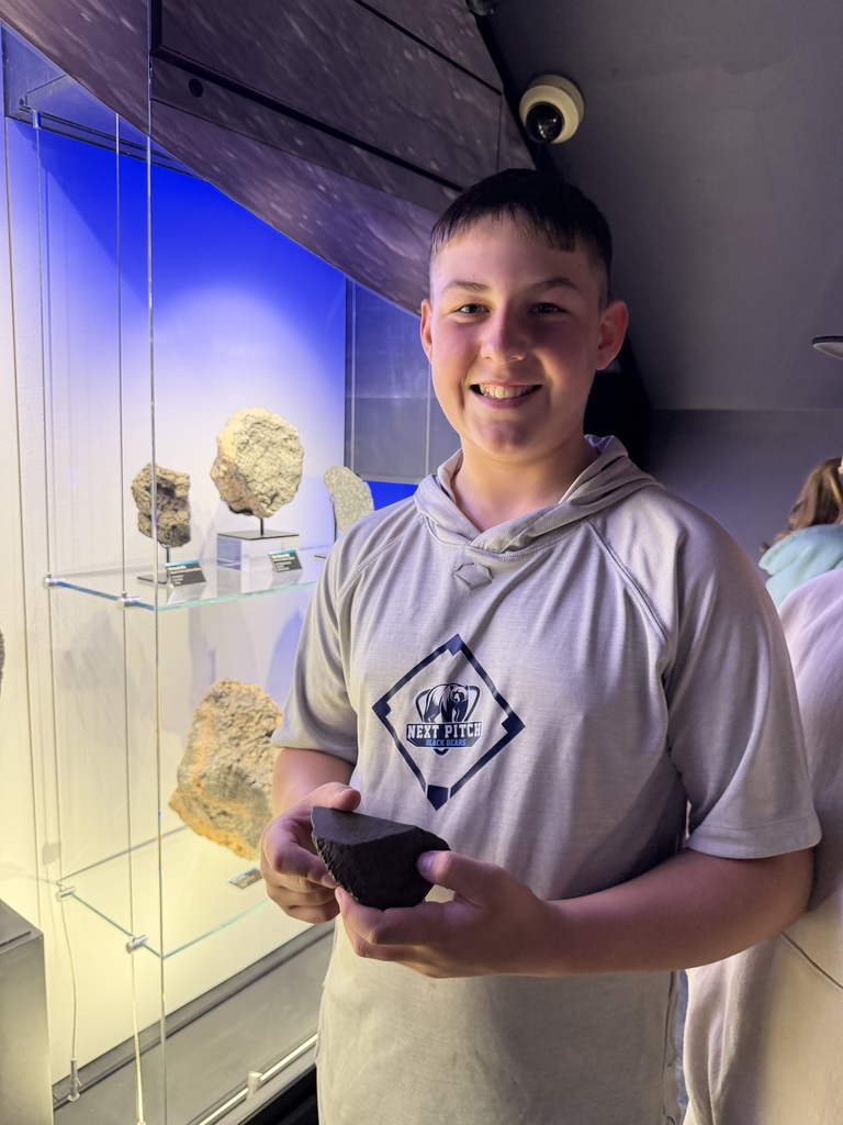 Student in museum holding rock sample, standing in front of display cases with more rocks
