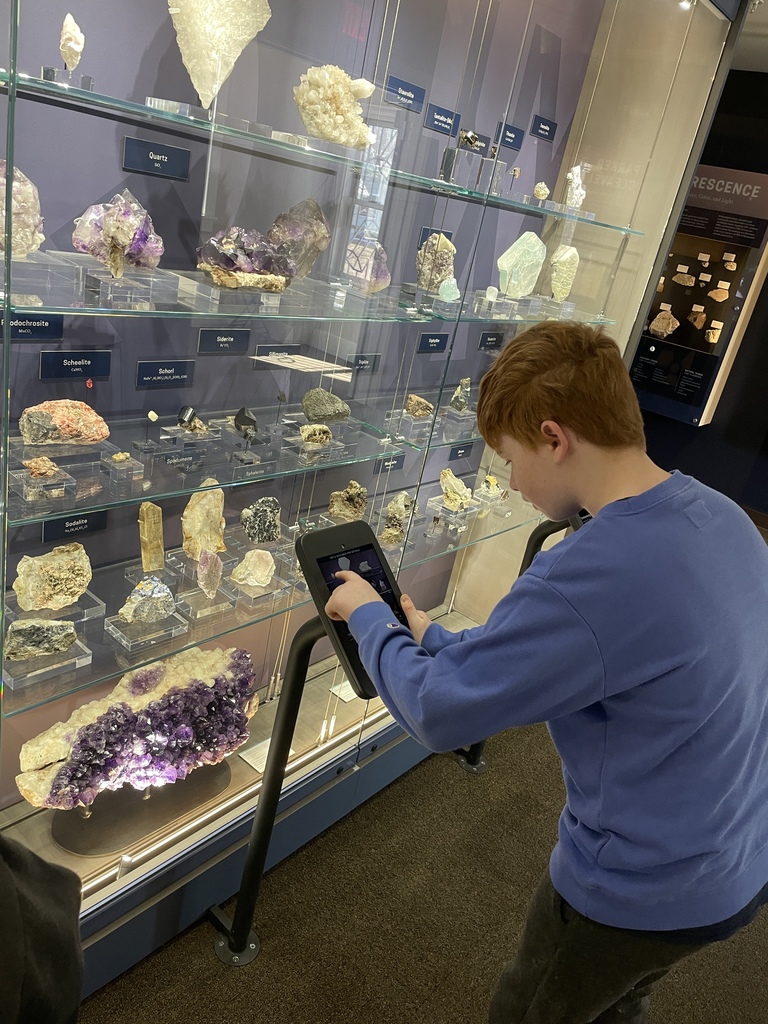 student interacting with tablet screen in front of display cases of minerals and gems in museum setting