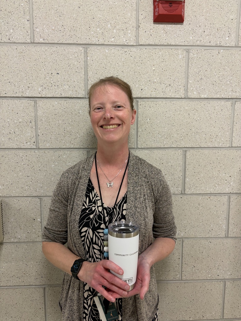 teacher smiling in school hallway holding a white coffee cup