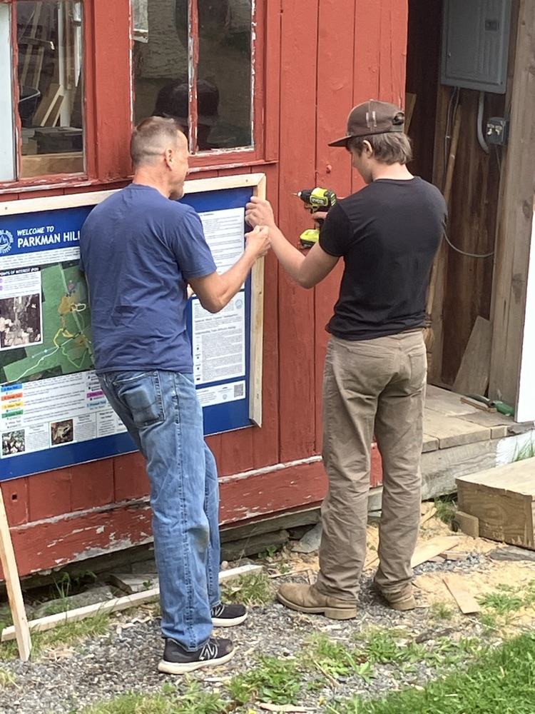 staff and a student drilling the hole to mount a sign on the building